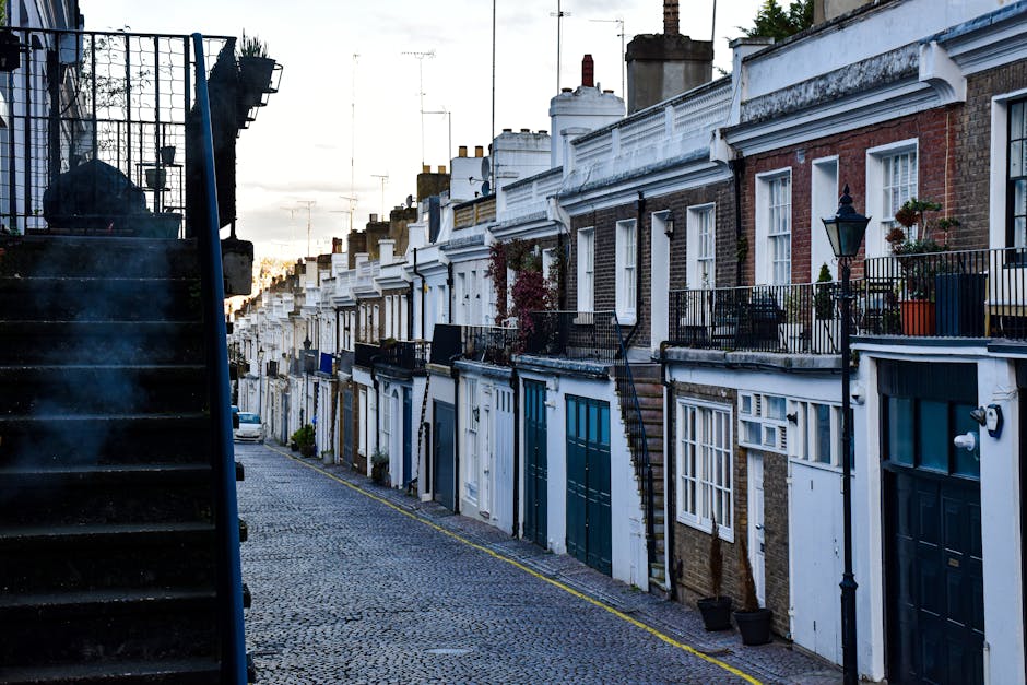 A narrow residential street in Finchley lined with terraced brick houses featuring small front gardens and sloped tiled roofs. The street surface is asphalt with some uneven patches and extends into t